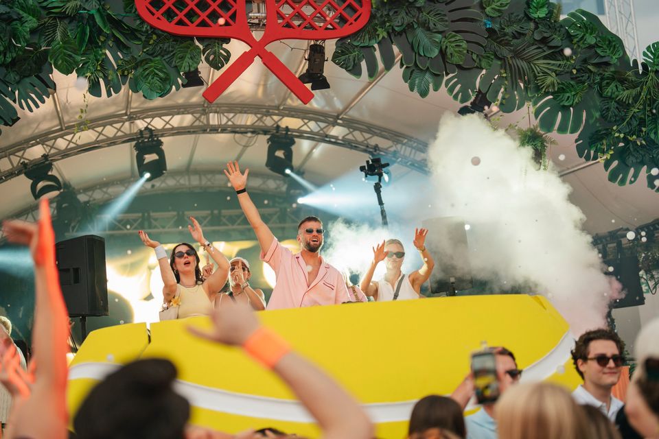 DJ jubelt im CO2-Nebel auf der Bühne, vorne recken Gäste die Hände