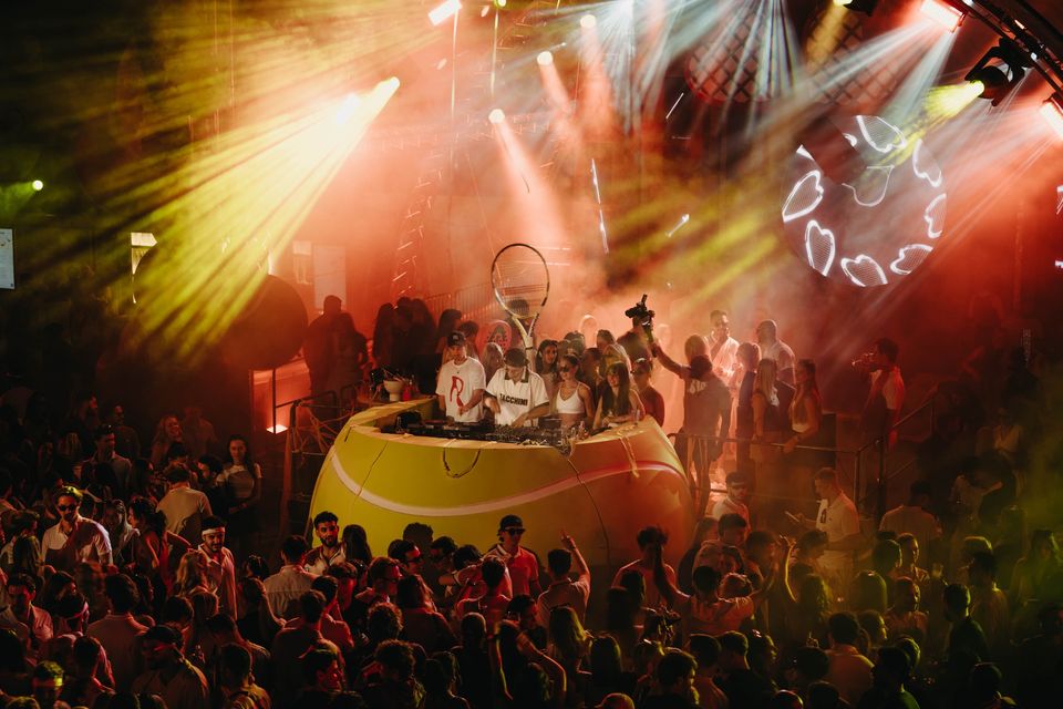 Nachts leuchtet das gelbe Ball-Pult, DJs und Crowd recken die Arme in Licht und Nebel