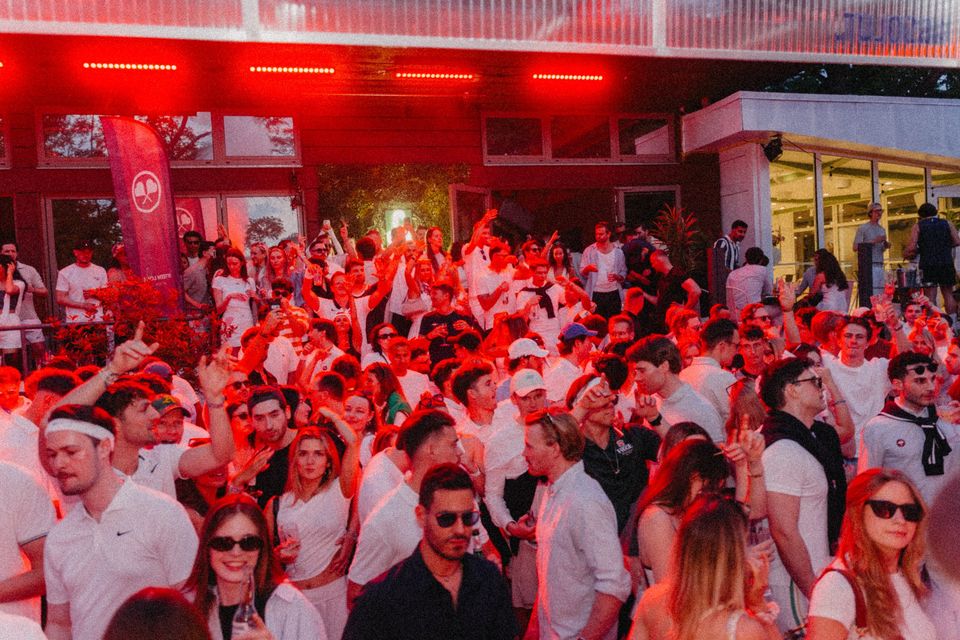 Dichte Crowd in Weiß mit erhobenen Armen im roten Bühnenlicht