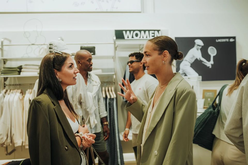 Gäste im Gespräch im Lacoste-Store, dahinter ein Tennis-Motiv an der Wand