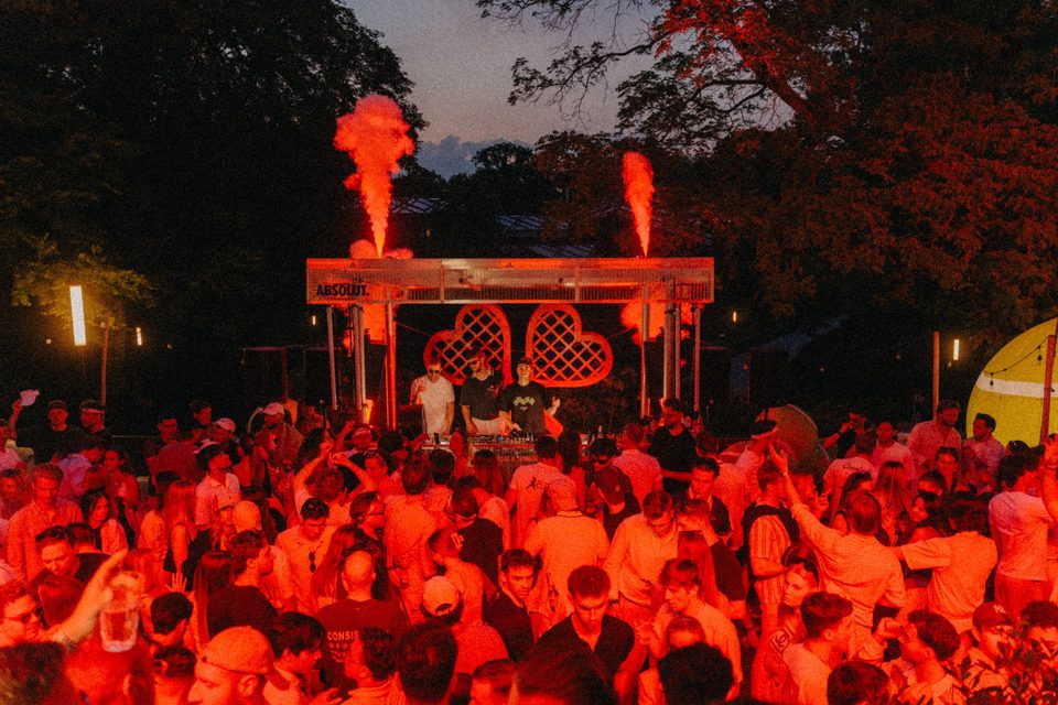 Gäste in Weiß feiern vor den zwei großen roten Herzschlägern unter der gläsernen Pergola bei der Tennis Party Hamburg 2026