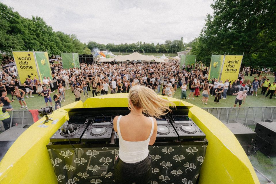 DJane wirft am Pult die Haare zurück, vor ihr springt die Crowd auf der Festivalwiese