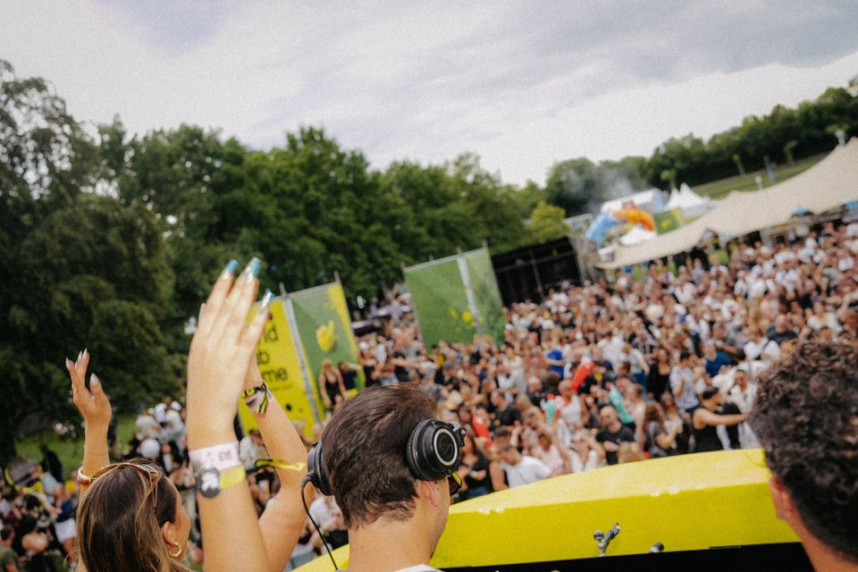 Hände in der Luft: Blick vom Pult über Gäste und DJ auf die dicht gefüllte Festivalwiese